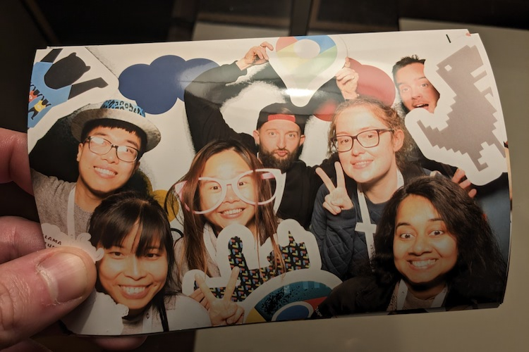 A hand holding a developed photo of GDEs and Googlers take photo in novelty photo booth holding various Google related items